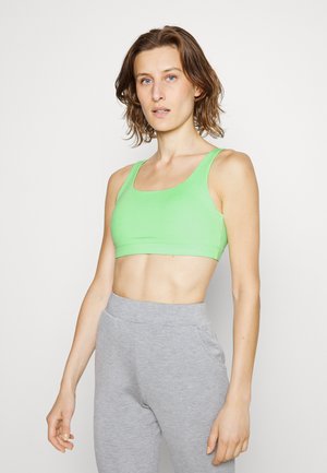 Sutiã desportivo verde com um design de decote em forma de U, feito de um tecido liso e elástico. Combinado com calças de treino ajustadas em cinza claro, com bolsos.
