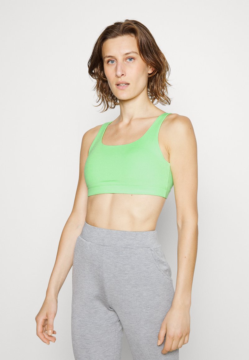 Sutiã desportivo verde com um design de decote em forma de U, feito de um tecido liso e elástico. Combinado com calças de treino ajustadas em cinza claro, com bolsos.