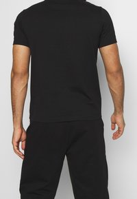 T-shirt nera a maniche corte realizzata in cotone. Presenta un colletto a girocollo, una forma aderente e una texture liscia senza pattern o loghi visibili.