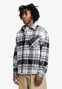 Chemise en flanelle à carreaux noirs et blancs avec un col boutonné, une poche poitrine et une coupe légèrement raccourcie. Tissu doux avec une finition texturée.