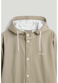 Beige regnjakke med hvid snøre i hætten, trykknapper foran og lille "TRETORN" logo på brystet.