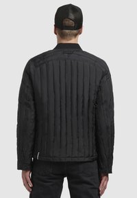 Black padded jacket with vertical stitching, ribbed collar, and snap button details. Textured surface, lightweight design, casual fit.