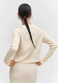 Suéter de punto acanalado beige con mangas largas, corte relajado y escote redondo, mostrado desde la espalda, con una textura suave.