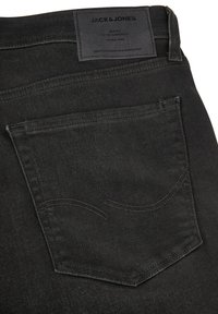 Jeans de mezclilla negra con una etiqueta de marca de cuero, bolsillo cosido con sutiles líneas curvas y una textura suave.