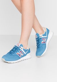 Baskets de sport bleues avec une surface texturée, des accents blancs, un design à lacets et un logo arborant des motifs géométriques colorés.
