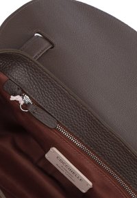 Borsa a tracolla in pelle marrone con un esterno testurizzato, dotata di chiusura con zip e un interno in tessuto rosso scuro, che mostra l'etichetta del marchio.