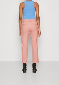 Rosa maßgeschneiderte Hosen mit geradem Schnitt, ausgestattet mit Gesäßtaschen und einem glatten Finish, kombiniert mit einem eng anliegenden blauen Tanktop.