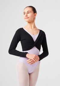 Schwarzes Langarm-Crop-Top mit einem gedrehten Vorderdesign, getragen über einem helllila Body, kombiniert mit hellen Strumpfhosen. Glatter Stoff, figurauschnittendes Design.