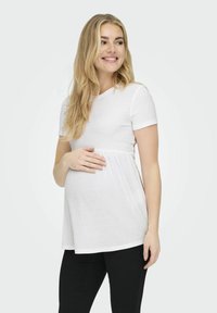 Těhotenský top z měkké bílé žebrované látky, krátké rukávy, rozšířený silueta a zvýrazněný empírový pas, v kombinaci s černými kalhotami.