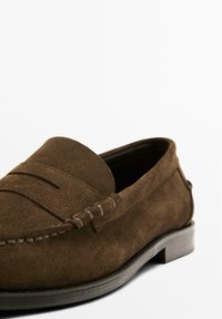 Brown suede loafers with a rounded toe, decorative stitching, and a low black rubber heel. Features a smooth texture and classic design.