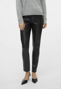 Pantalons skinny en simili cuir noir avec une texture lisse, taille haute et longueur cheville, associés à des chaussures à talons aiguilles noires.