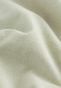 Gros plan d'un tissu tissé beige clair avec une surface fine et texturée et des plis doux créant des ombres douces.