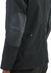 Zwarte jas met een matte afwerking en een glad leren elleboogpatch. Voorzien van een knoopsluiting en een getailleerd ontwerp.