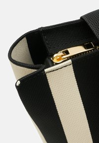 Torba w czarno-białe paski, wykonana z teksturowanego materiału, z metalowym zamkiem w złotym kolorze i usztywnionym kształtem przy otwarciu.