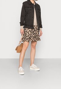 Svart denimjacka, beige stickad tröja, beige kjol med svart blommönster, brun handväska och vita sneakers med bruna detaljer.