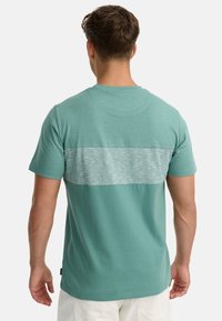 Mintgrøn t-shirt med et horisontalt gråt stribet panel på ryggen, lavet af blødt bomuldsstof med en glat tekstur.