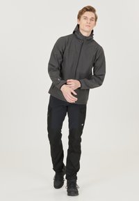 Sort softshell jakke med lynlås foran og hætte, parret med sorte cargo bukser med flere lommer og et kontrasterende design ved knæene.