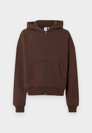 Pruun lukkudega kapuutsiga dressipluus esidetaskute, soonikkoes mansettide ja külge õmmeldud kapuutsiga, esitleb neutraalsel taustal.