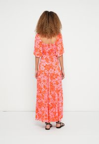 Maxi kleita spilgti oranžā krāsā ar rozā ziedu rakstu, brīva piegriezuma, īsām piedurknēm, ar smocētiem detaļām aizmugurē, kombinēta ar melnām sandales ar siksnām.