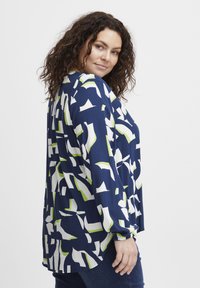Blusa blu navy con un motivo geometrico in bianco e verde, con maniche lunghe, vestibilità comoda e polsini arricciati. Tessuto con una trama liscia.