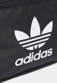 Μαύρη υφασμάτινη τσάντα με μεγάλο λευκό λογότυπο trefoil της Adidas και την επωνυμία σε έντονες γραμμές. Με υφή και κλείσιμο με φερμουάρ.