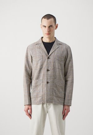 Plaid jacket in shades of beige and brown, featuring a lapel collar, two front pockets, and button closures. Material has a textured finish.