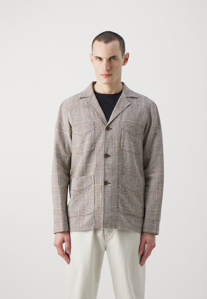 Plaid jacket in shades of beige and brown, featuring a lapel collar, two front pockets, and button closures. Material has a textured finish.