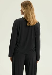 Czarna koszula z długim rękawem o luźnym kroju, miękkiej teksturze i okrągłym dekolcie, w zestawie z pasującymi czarnymi spodniami.