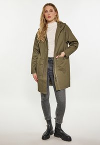 Parka verde oliva con chiusura a zip, tasche frontali e cappuccio con coulisse, abbinata a jeans skinny grigi e stivaletti neri.