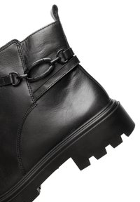 Stivale alla caviglia in pelle nera con suola spessa e dettagli decorativi in catena metallica sulla parte superiore.