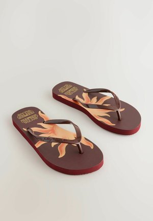 Bruine teenslippers met een gestructureerde zool, met een zonafbeelding in oranje en geel op een kastanjebruine achtergrond, en bruine plastic banden.