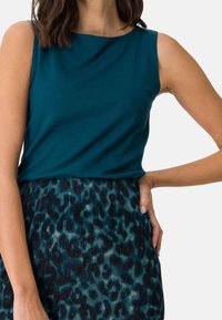 Teal bezrękawnik z okrągłym dekoltem, połączony z fakturowaną, ciemnozieloną spódnicą z wzorem w panterkę.