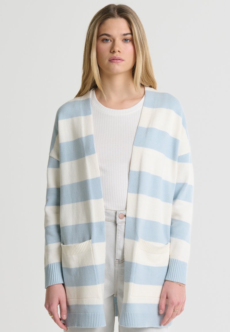 Juostuotas švarkas šviesiai mėlynos ir grietinėlės spalvos, su laisvu fasonu, ilgomis rankovėmis, patemptais rankogaliais ir dviem priekinių kišenių. Minkšta mezgimo tekstūra.