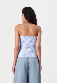 Top corto senza spalline in tessuto blu chiaro con motivo floreale, texture liscia e design aderente. Indossato con pantaloni in denim blu chiaro a gamba larga.
