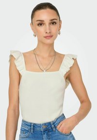 Ribbet hvid tanktop med firkantet udskæring og voluminøse skulderstropper, kombineret med blå højtaljede denimjeans. Minimalistisk sølvsmykke.