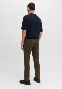 Polo de punto azul marino con mangas cortas, combinado con pantalones marrones y zapatos oscuros, visto desde la parte posterior sobre un fondo liso.