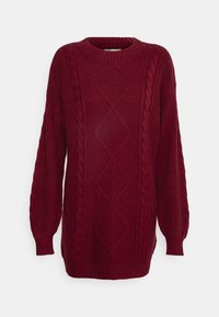 Maglione a maniche lunghe color bordeaux a lavorazione a cavo con motivo a rombi al centro e colletto, polsi e orlo a coste su sfondo bianco.