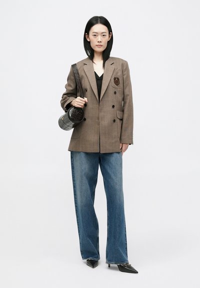 Blazer cu carouri maro, cu două rânduri de nasturi și emblemă, top negru, blugi largi bleumarin, pantofi cu vârf ascuțit negri și o geantă circulară gri.