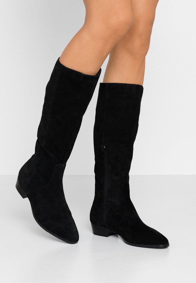 Czarne zamszowe botki do kolan z ostrym noskiem, teksturowanym wykończeniem i bocznym zamkiem błyskawicznym. Niski, blokowy obcas zapewnia stabilność i komfort noszenia.