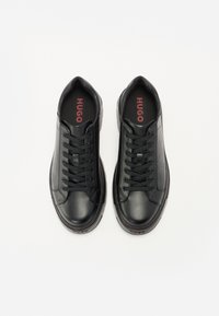 Baskets en cuir noir avec une finition texturée, arborant un design à lacets, un col rembourré et un logo rouge contrastant. Embout lisse et arrondi.