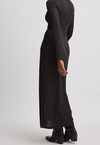 Robe longue à manches longues noire côtelée, coupe droite, longueur mi-mollet et texture subtile, associée à des bottines noires montant jusqu'à la cheville.