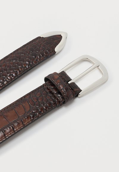 Σκούρα καφέ δερμάτινη ζώνη με υφή κροκόδειλου, ασημένια μεταλλική πόρπη και ασημένια μύτη στην αντίθετη άκρη, σε απλό λευκό φόντο.