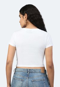 T-shirt bianca corta a maniche corte, realizzata in un tessuto morbido, abbinata a jeans in denim blu chiaro con tasche posteriori e un'etichetta marrone.
