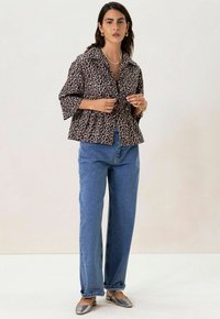 Veste à boutons en imprimé léopard avec col, manches courtes et ourlet peplum ; associée à un jean en denim bleu taille haute et des ballerines argentées.