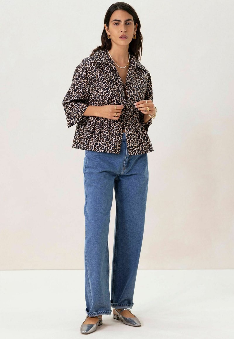 Veste à boutons en imprimé léopard avec col, manches courtes et ourlet peplum ; associée à un jean en denim bleu taille haute et des ballerines argentées.