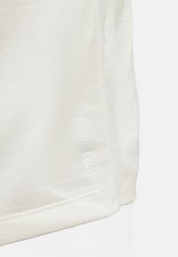 T-Shirt de sport beige clair avec une texture lisse, présentant un logo "CLIMACOOL" embossé sur l'ourlet et des détails de couture subtils.
