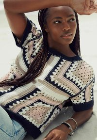 Gestrickter Pullover mit geometrischen Mustern in Marineblau, Rosa und Creme. Kurzärmlig, texturiertes Gewebe mit offenem Webmuster und kontrastierenden Farben.