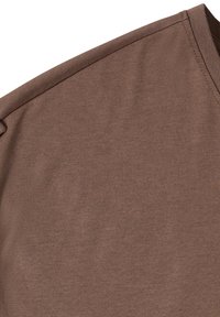 Gros plan sur un tissu marron montrant la couture de l'épaule et de la manche d'un vêtement uni à manches courtes.