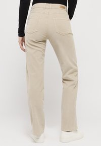 Beige corduroy trousers with a straight-leg cut, featuring two back pockets and a small brand label on the waistband. Smooth texture.