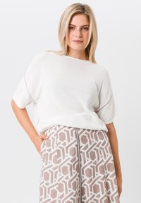 Lichtgewicht witte gebreide top met korte mouwen, gecombineerd met een patroonbeige rok met geometrische ontwerpen en een zichtbare rits.
